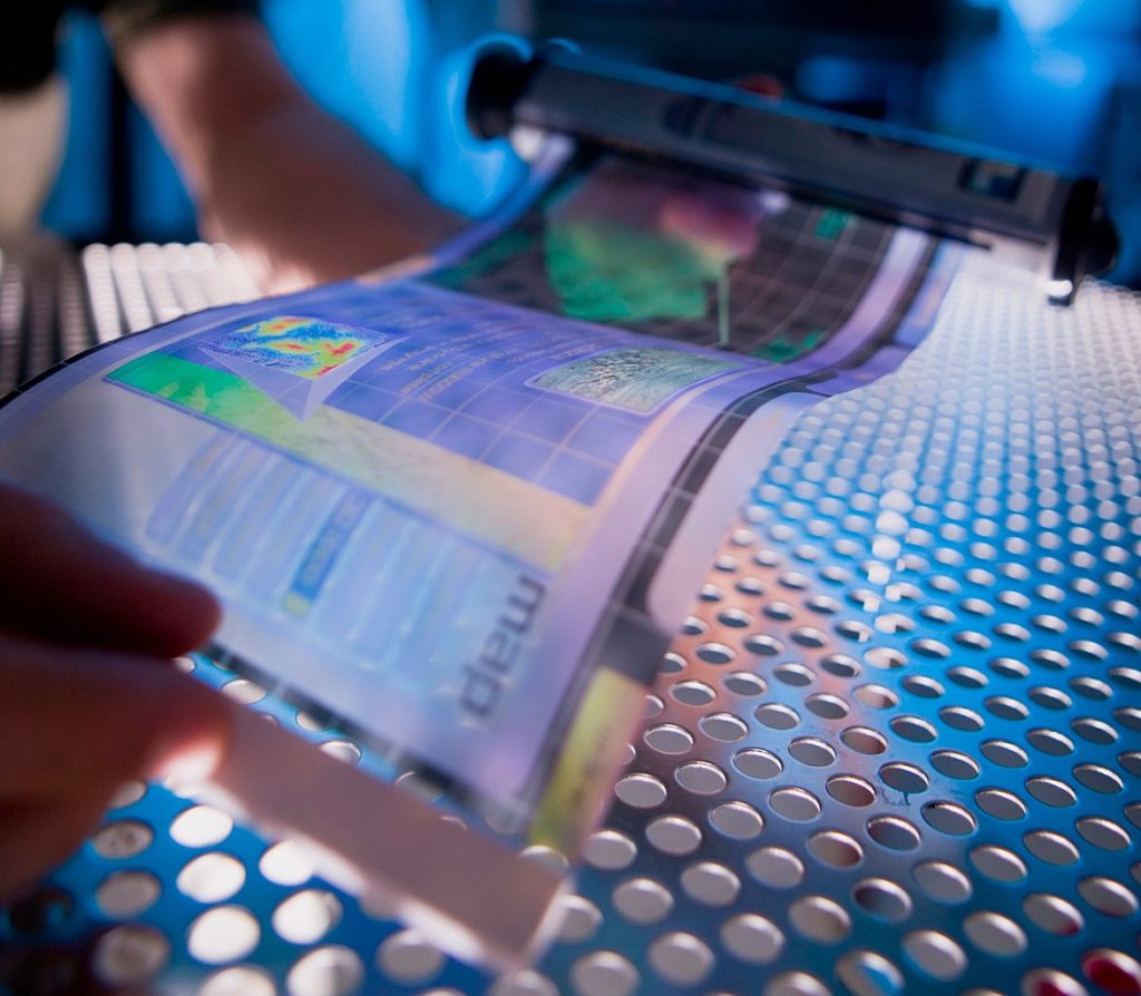 Hand holds a flexible printed display of a colorful map.
