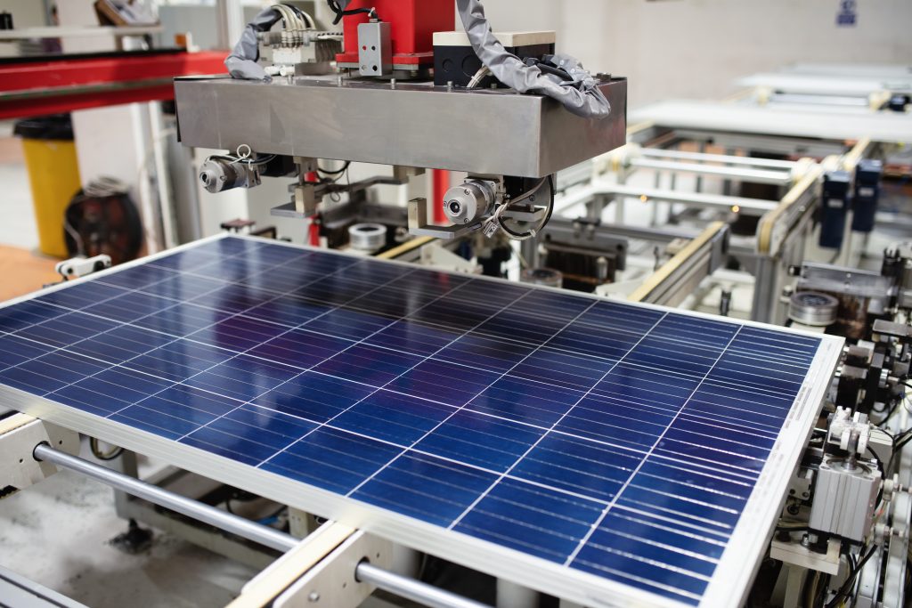 A solar panel sits on a mechanical platform for automated assembly.