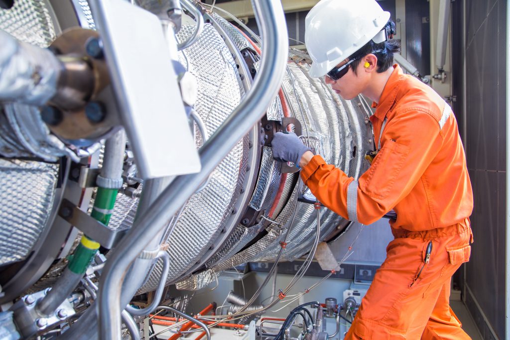 Turbine technician wearing personal protective equipment inspects a gas turbine engine