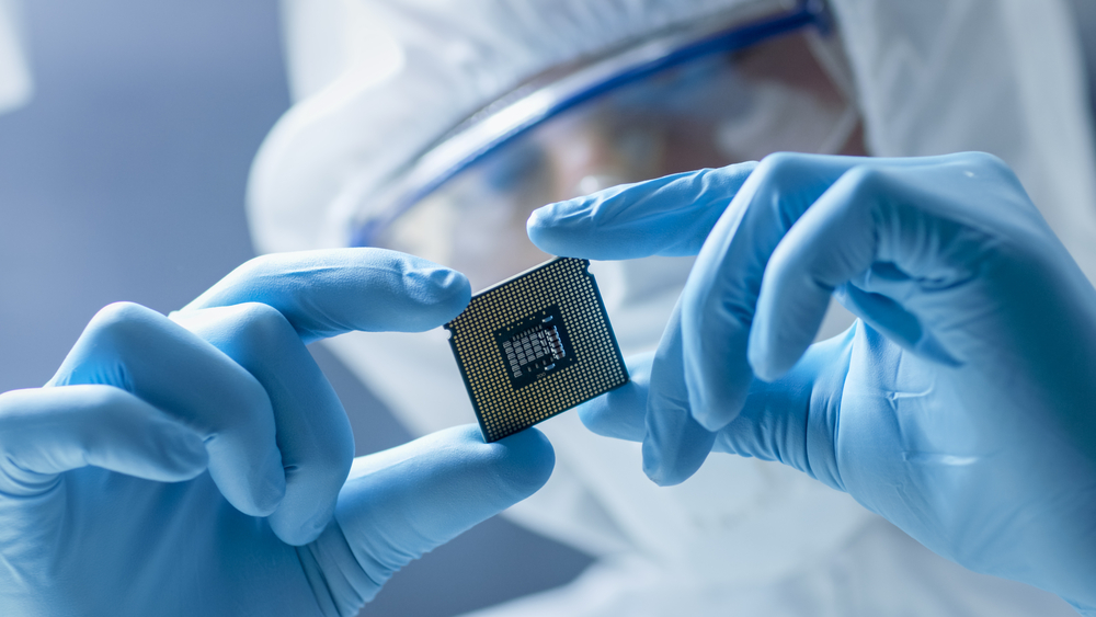 Modern Electronic Manufacturing. Factory Design Engineer in Sterile Coverall Holds Microchip with Gloves and Examines it.