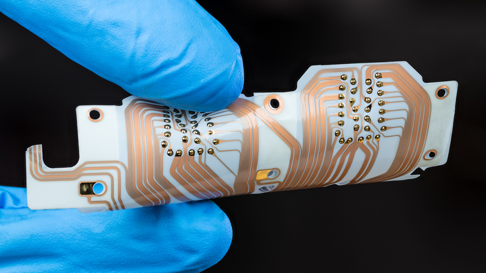 Blue gloved fingers gripping a flexible circuit board on a black