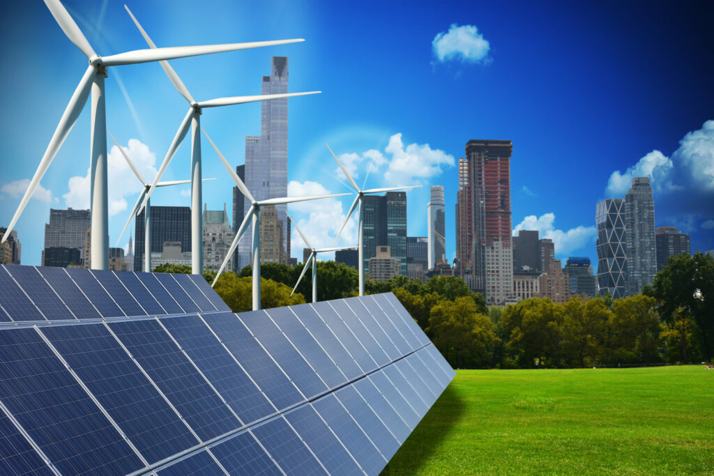 Wind turbines and solar panels against a field with a city in the immediate background